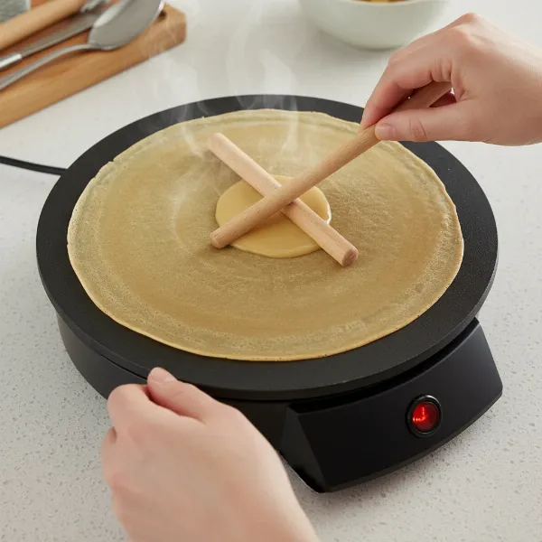 Hands using wooden T-stick spreader to make thin crepes on Orbegozo CM2360